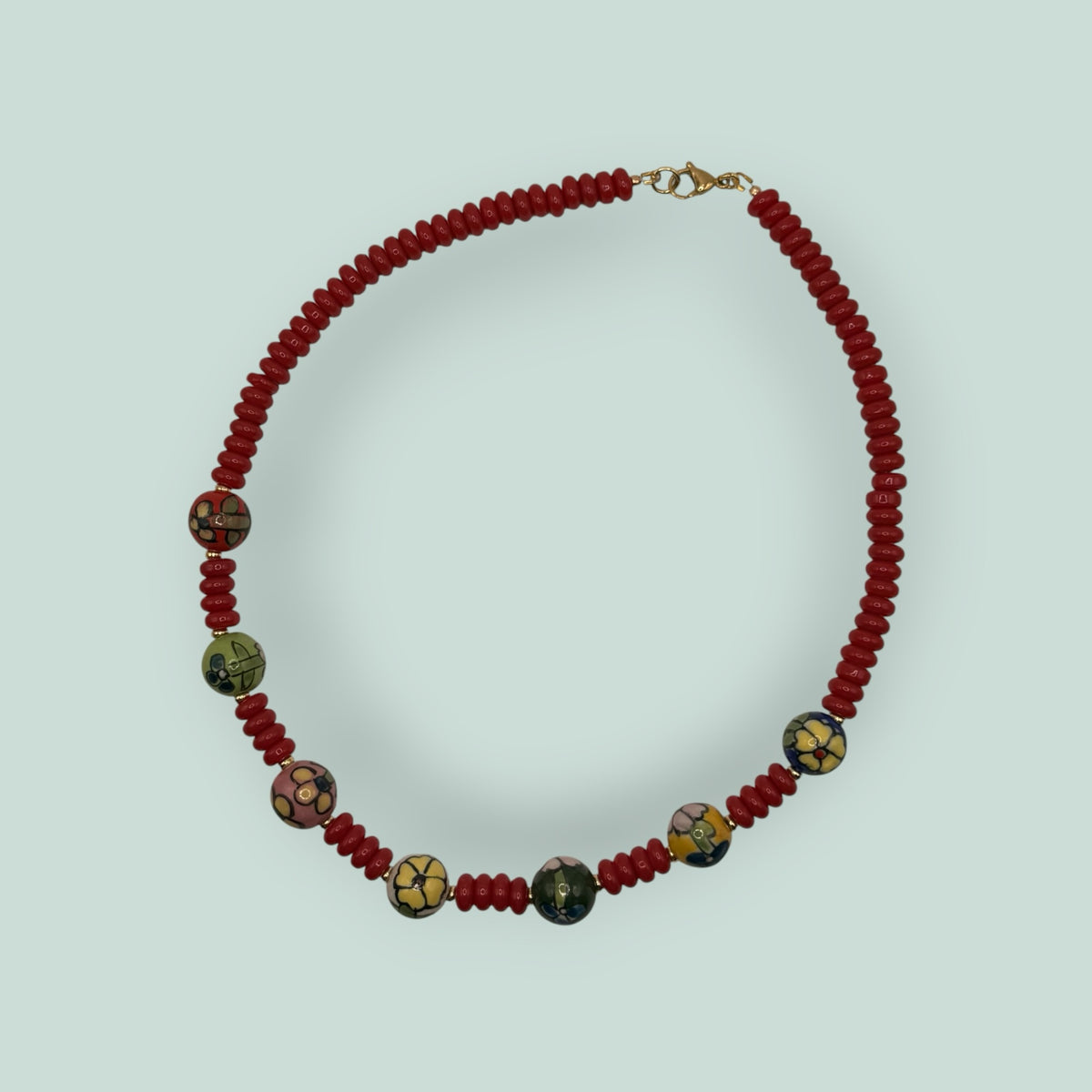 The Salty Bead Co handcrafted necklace with red disc beads and hand-painted floral ceramic accents on gold-tone clasp