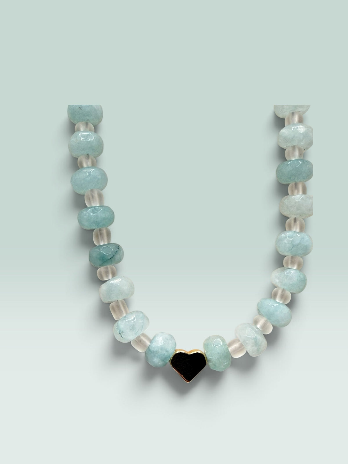 The Salty Bead Co beaded necklace with aquamarine-toned faceted beads, clear spacers, and a gold-tone heart charm.