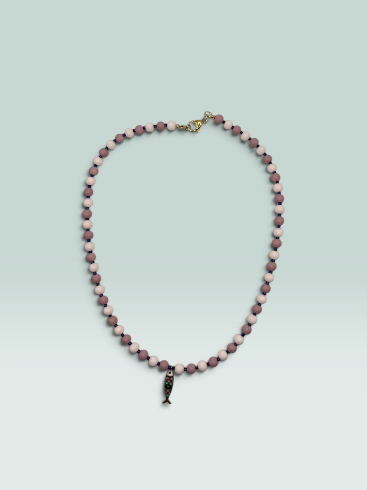 The Salty Bead Co handcrafted necklace with mauve and pink matte beads, blue spacers, and a colorful enamel fish charm.