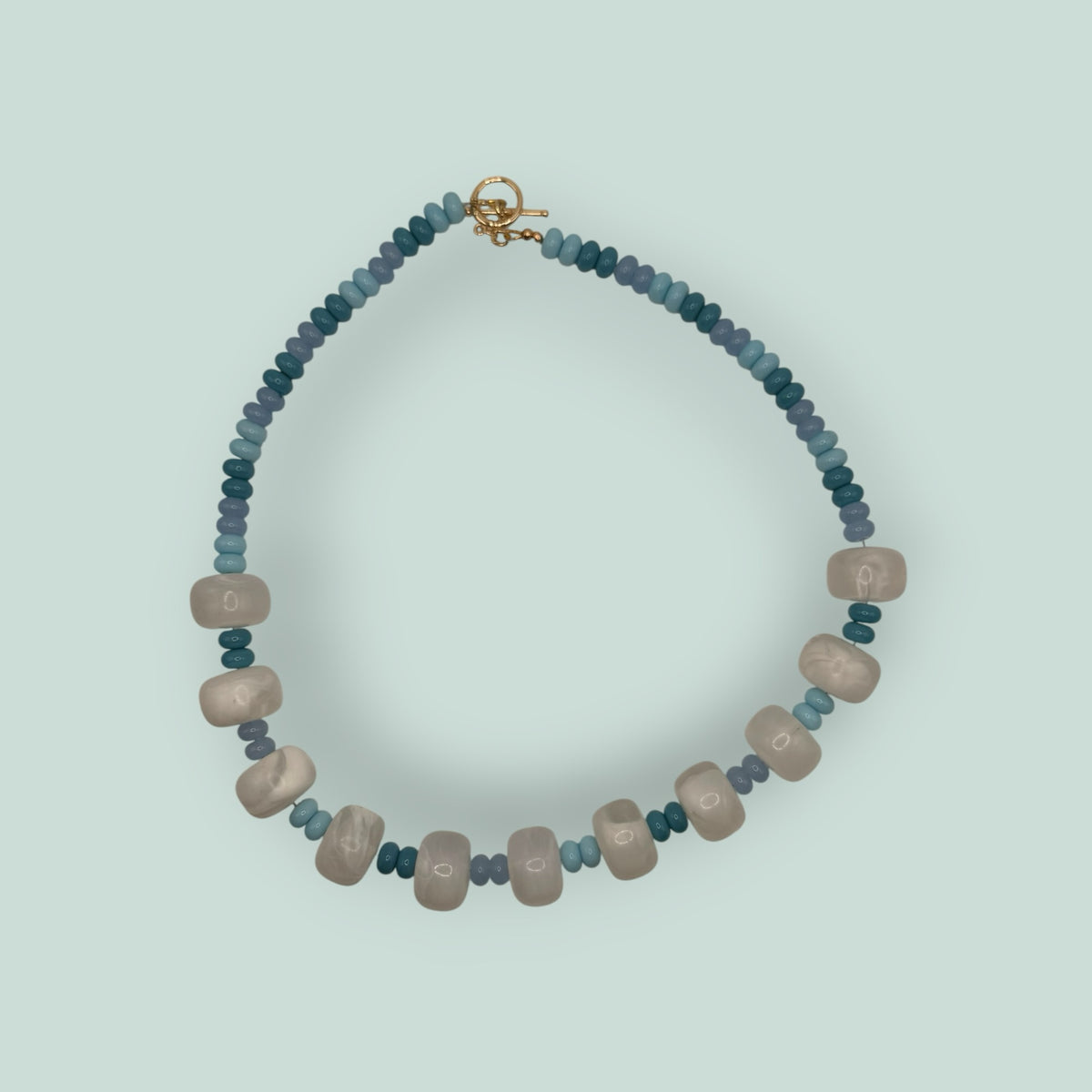 The Salty Bead Co handcrafted statement necklace with marbled cream beads and blue teal accents with a gold toggle