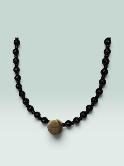 The Salty Bead Co minimalist necklace featuring polished black beads and a textured gold-tone center disc accent.
