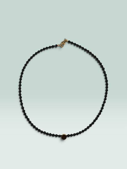 The Salty Bead Co minimalist black beaded necklace featuring a small textured gold-tone center disc accent