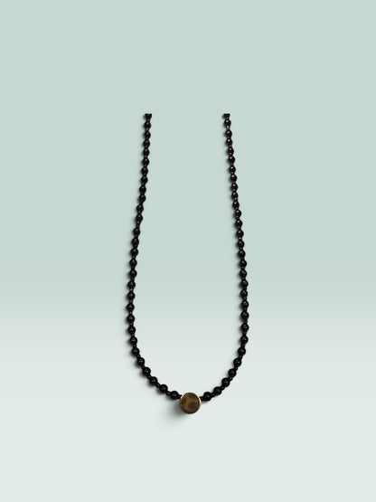 The Salty Bead Co minimalist necklace featuring polished black beads and a central textured gold-tone disc accent.