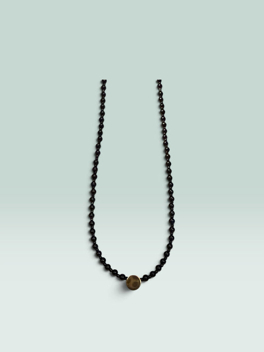 The Salty Bead Co minimalist necklace featuring polished black beads and a central textured gold-tone disc accent.