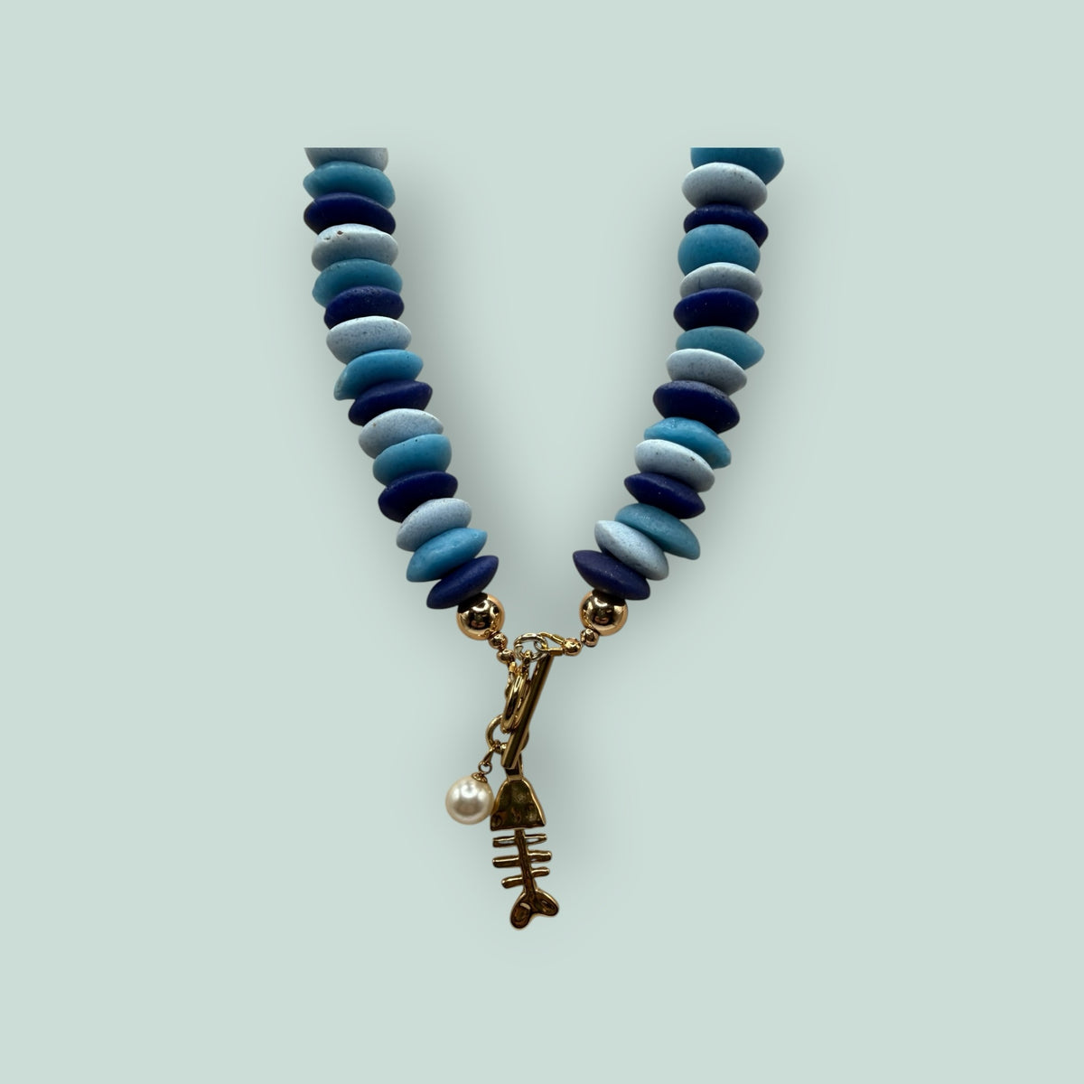The Salty Bead Co handcrafted necklace with blue disc beads, gold toggle clasp, fish skeleton charm, and faux pearl.