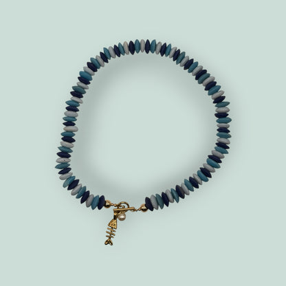 The Salty Bead Co handcrafted necklace featuring blue disc beads, a gold fish skeleton charm, and a faux pearl accent.