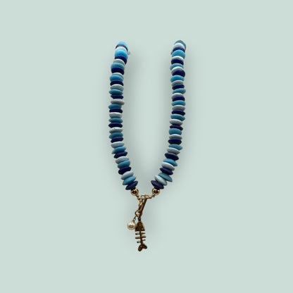 The Salty Bead Co handcrafted necklace with blue disc beads, gold toggle clasp, fish skeleton charm, and faux pearl.