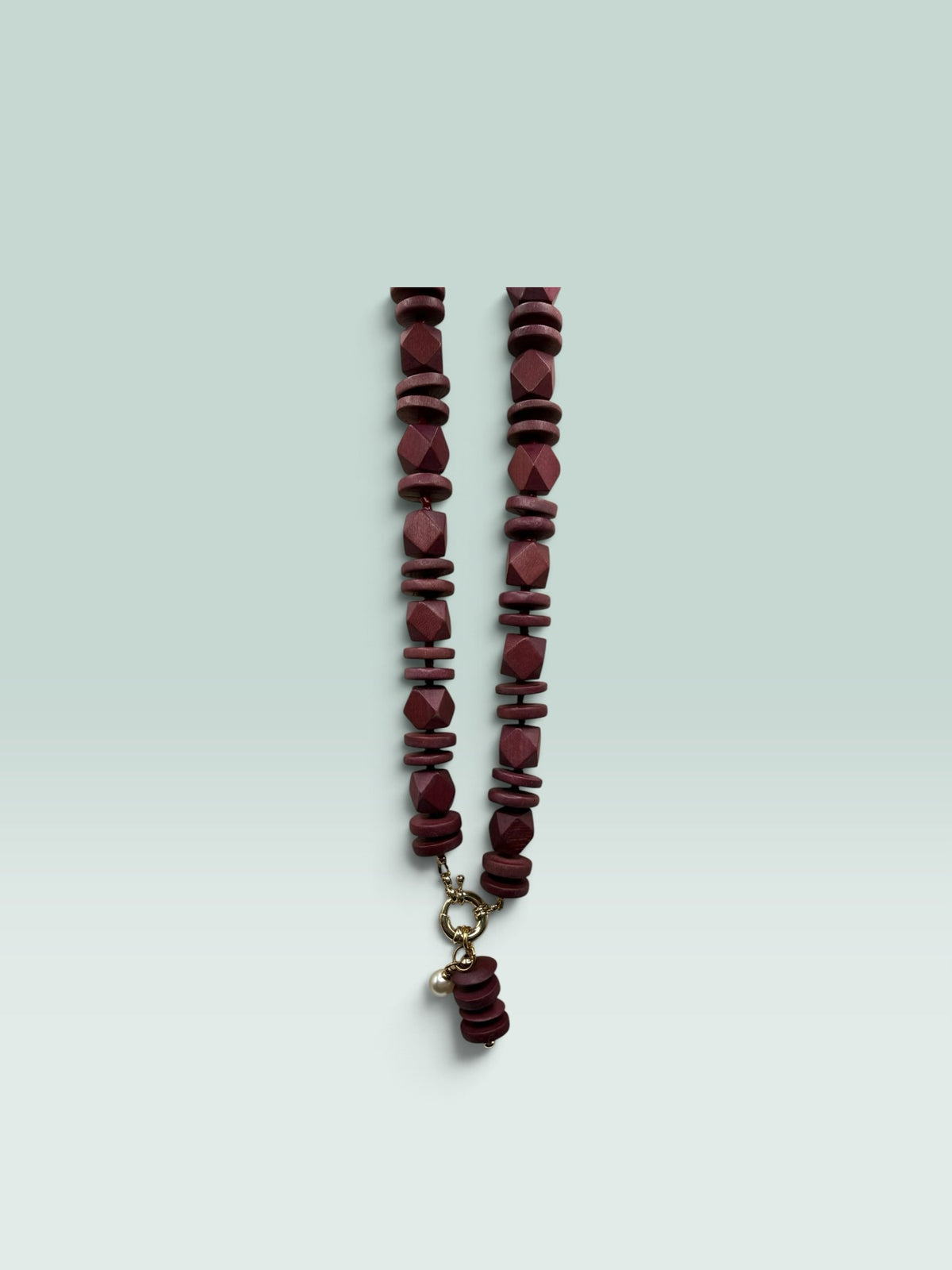 The Salty Bead Co handcrafted burgundy wooden bead statement necklace with a gold clasp and small pearl charm.