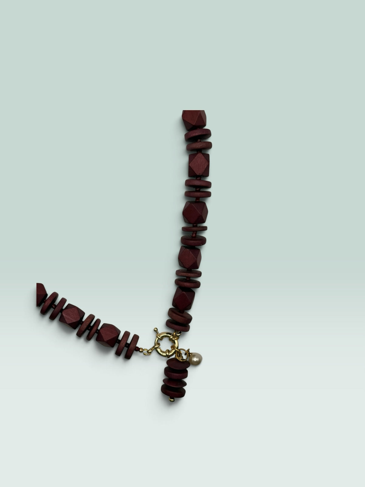 The Salty Bead Co burgundy wooden bead statement necklace with a gold clasp and a small pearl charm.