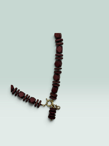 The Salty Bead Co burgundy wooden bead statement necklace with a gold clasp and a small pearl charm.