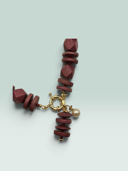 The Salty Bead Co handcrafted burgundy wooden bead statement necklace with a gold clasp and delicate pearl charm.