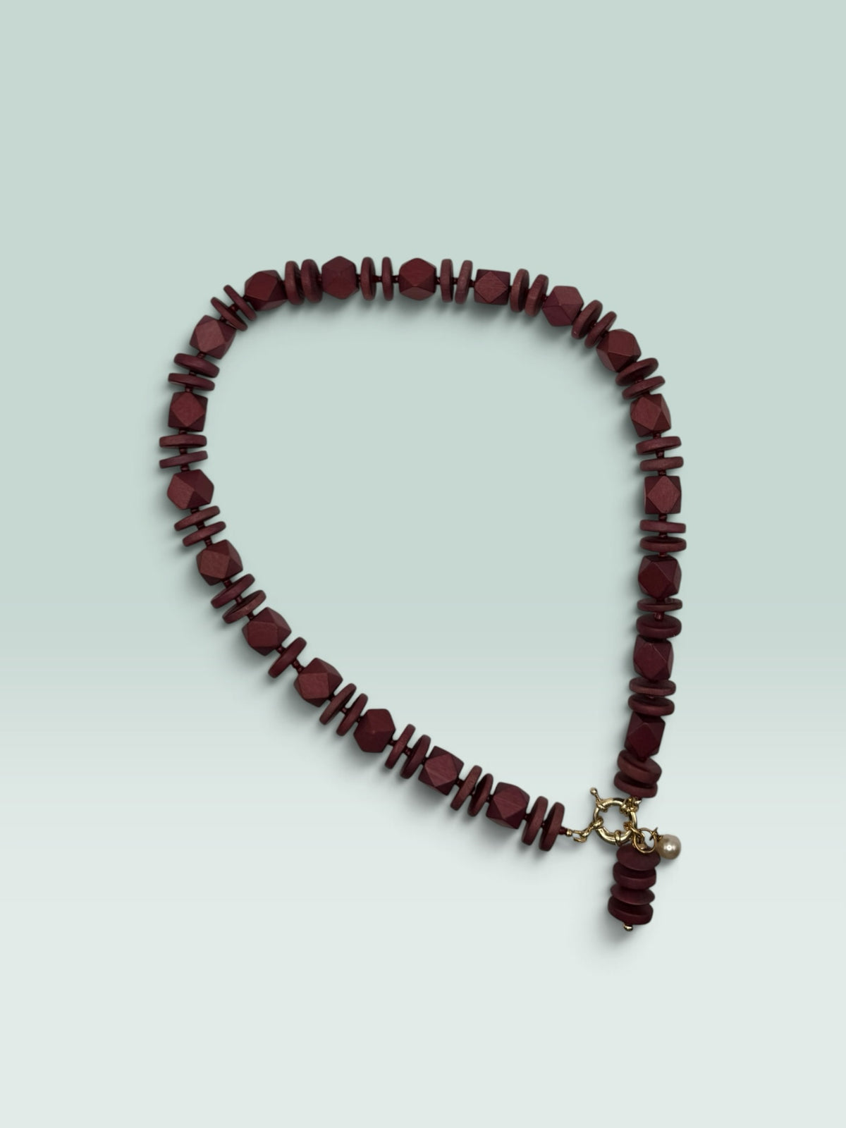 The Salty Bead Co handcrafted burgundy wooden bead statement necklace with a gold clasp and small pearl charm.