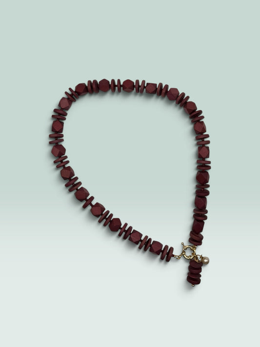 The Salty Bead Co handcrafted burgundy wooden bead statement necklace with a gold clasp and small pearl charm.