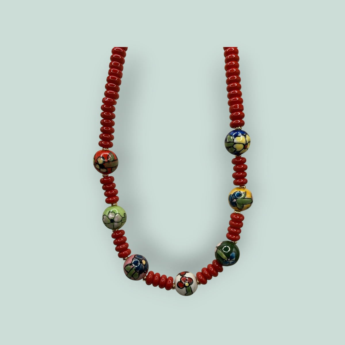 The Salty Bead Co handcrafted necklace featuring red disc beads and hand-painted ceramic floral focal beads.
