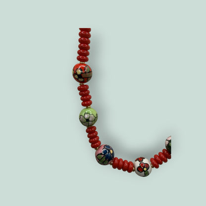 The Salty Bead Co handcrafted necklace featuring red disc beads and hand-painted ceramic floral accent beads.