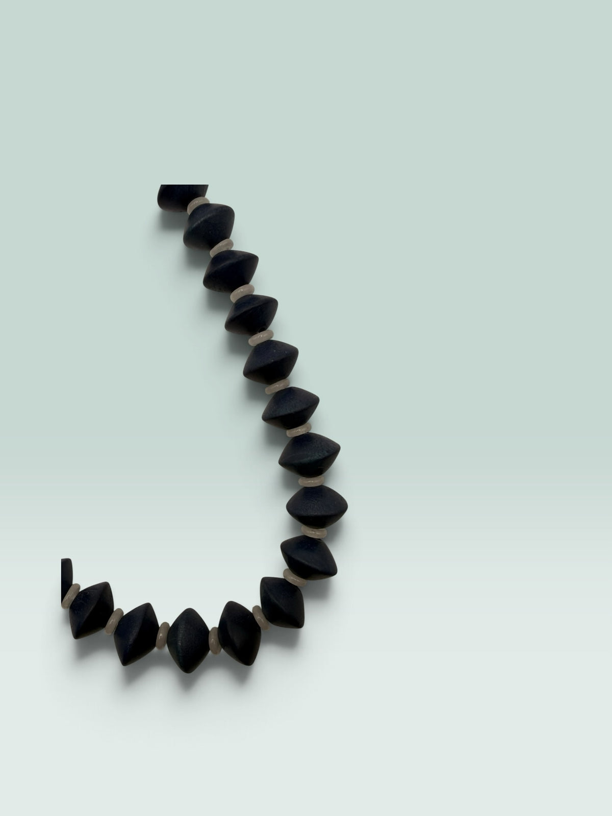 The Salty Bead Co handcrafted statement necklace featuring matte black geometric bicone beads and neutral spacers.