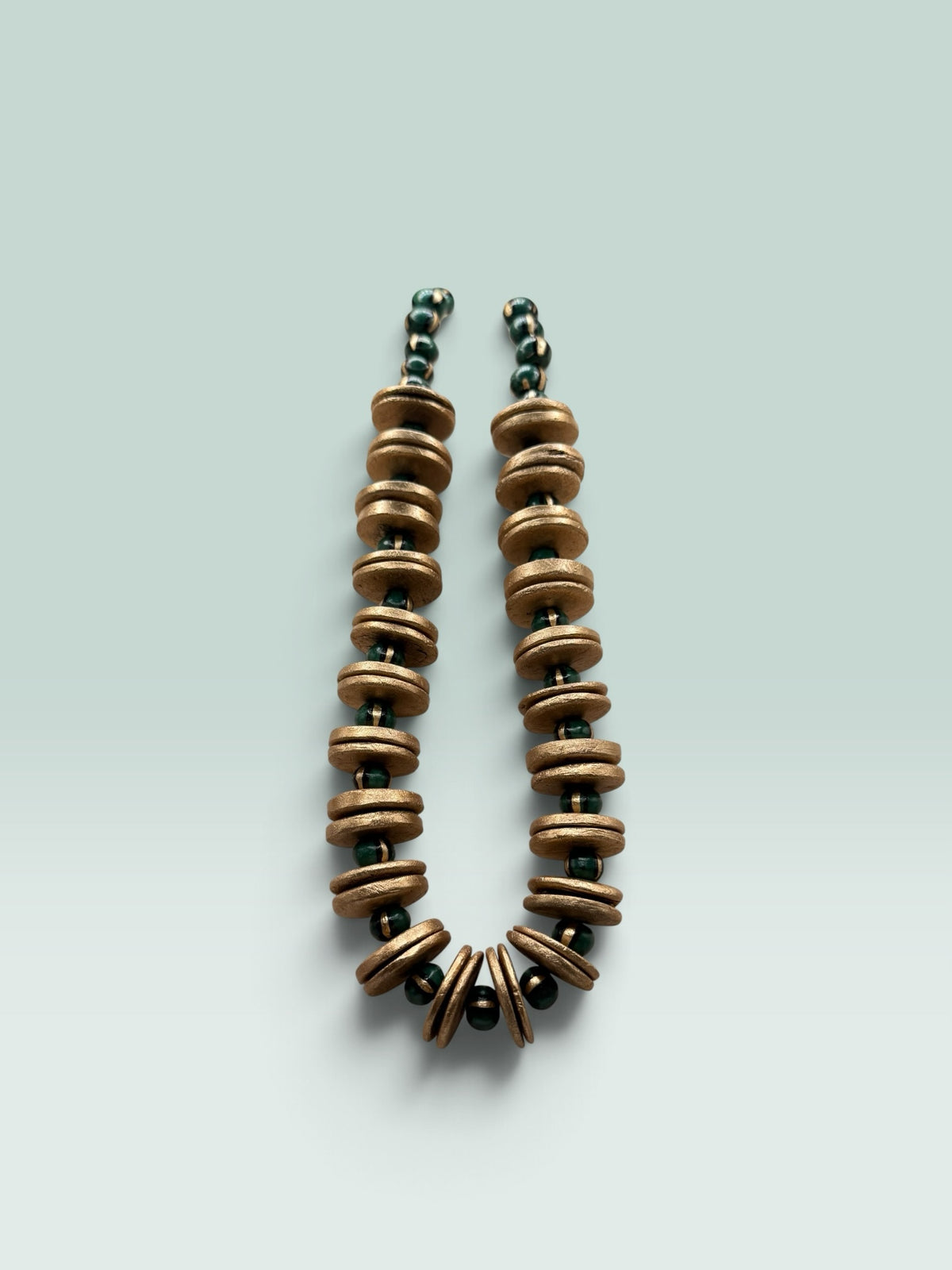 The Salty Bead Co artisan statement necklace featuring textured gold-toned discs and forest green beads