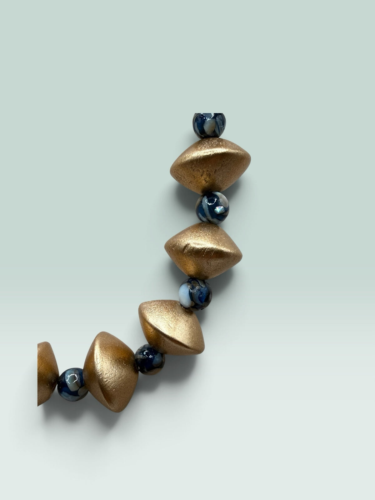 The Salty Bead Co statement necklace with matte gold geometric beads and dark marbled spheres on a light background.