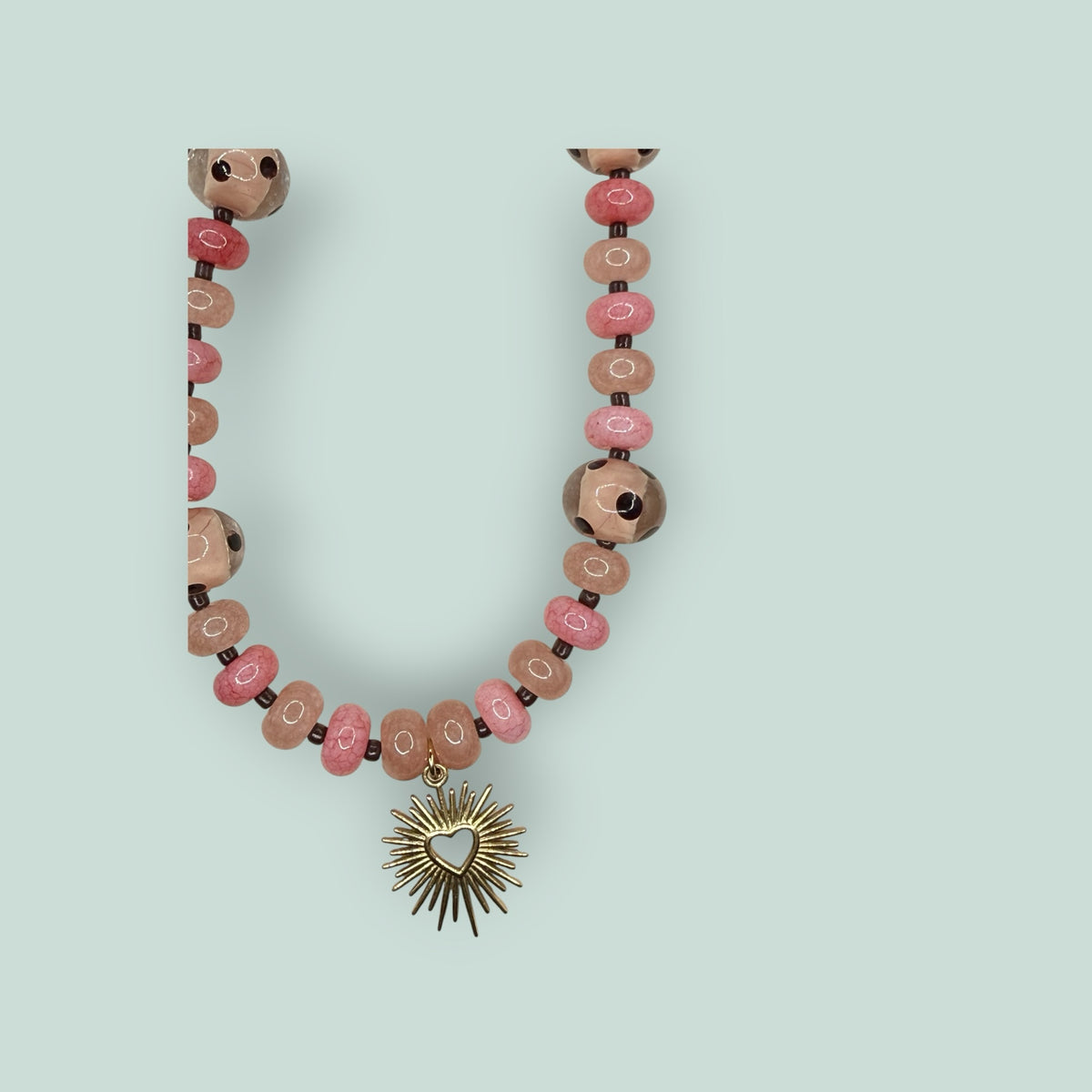 The Salty Bead Co beaded necklace featuring pink and rose round beads with a gold-tone sunburst heart pendant.