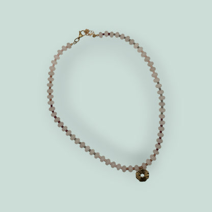 The Salty Bead Co handcrafted necklace with pale pink gemstone beads, dark red accents, and a gold sunburst pendant.