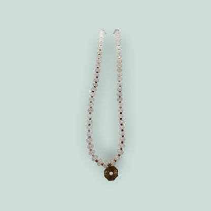 The Salty Bead Co handcrafted necklace with pale pink gemstone beads, dark red accents, and a gold sunburst pendant.