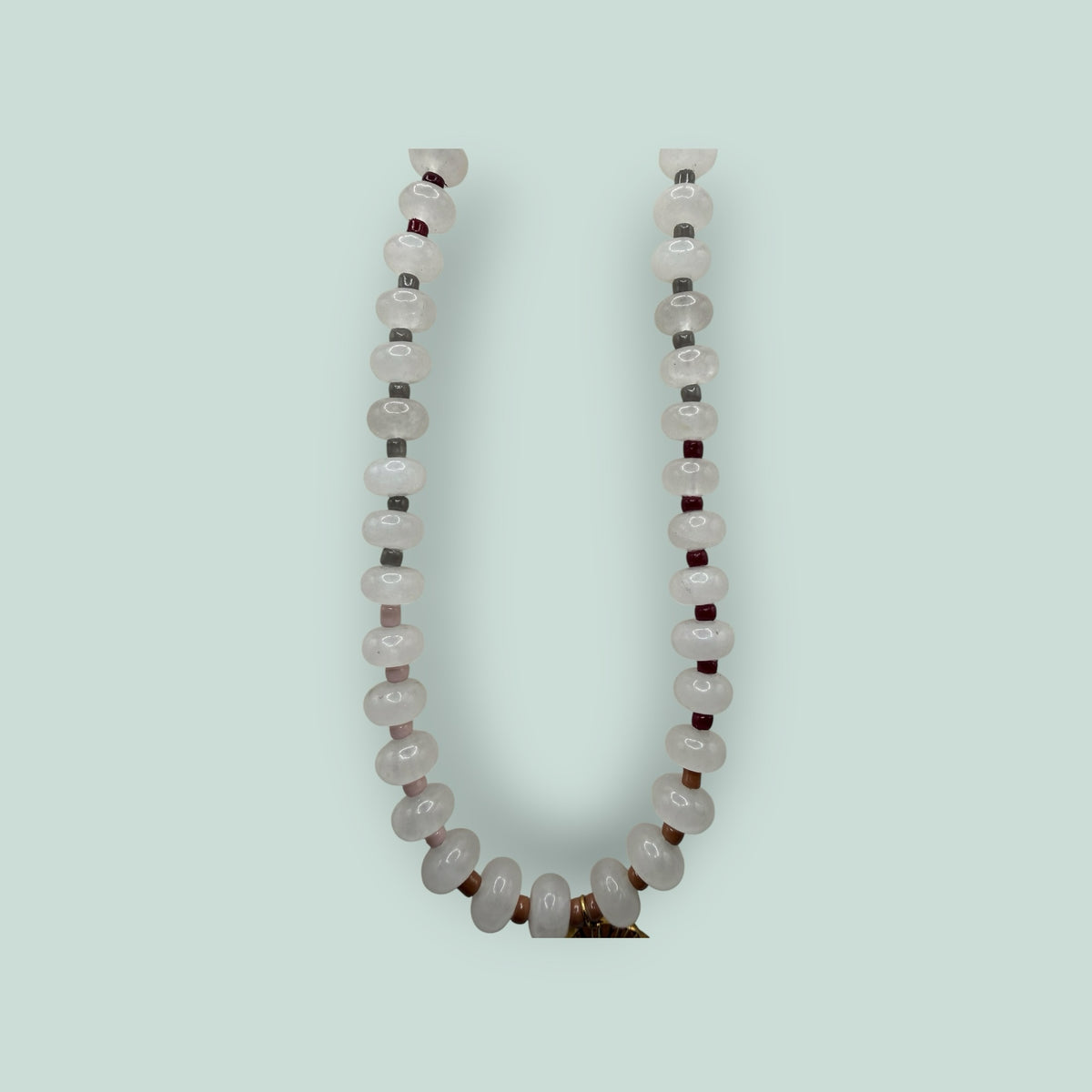 The Salty Bead Co handcrafted necklace with pale pink gemstone beads, dark red accents, and a gold-tone sunburst charm.