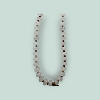 The Salty Bead Co handcrafted necklace with pale pink gemstone beads, dark red accents, and a gold-tone sunburst charm.