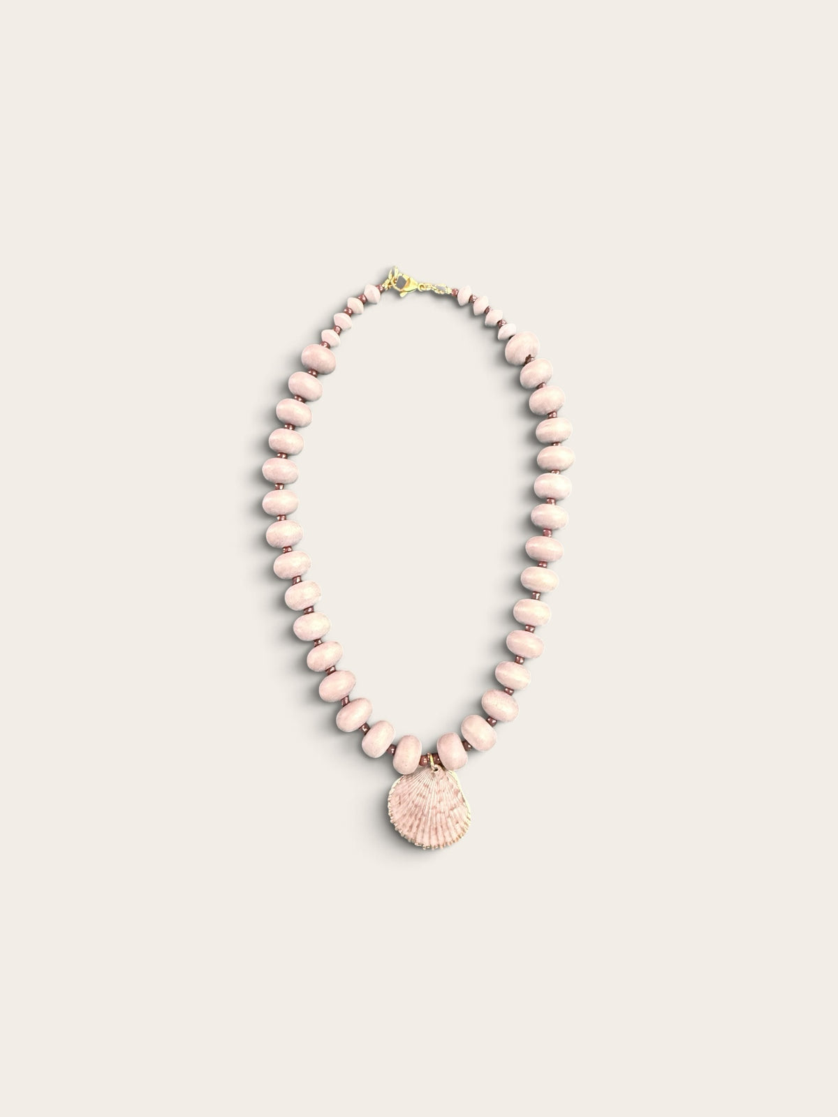 The Salty Bead Co coastal necklace with dusty-pink matte beads and a gold-edged natural seashell pendant.