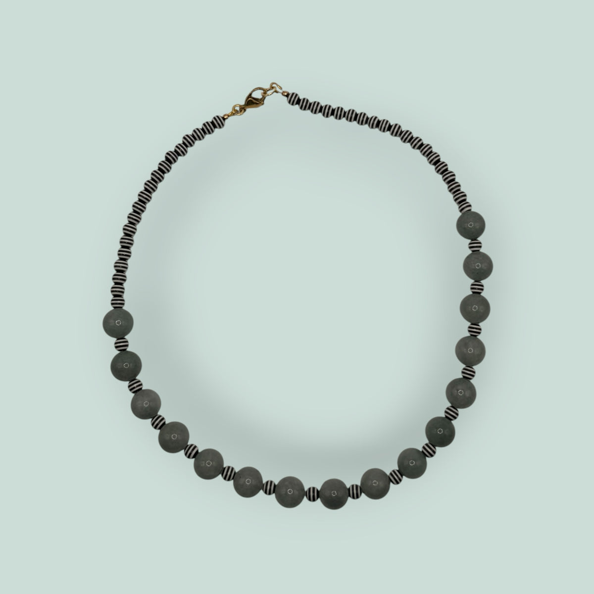 The Salty Bead Co handcrafted statement necklace featuring sage-green stone beads and black-and-white striped accents.