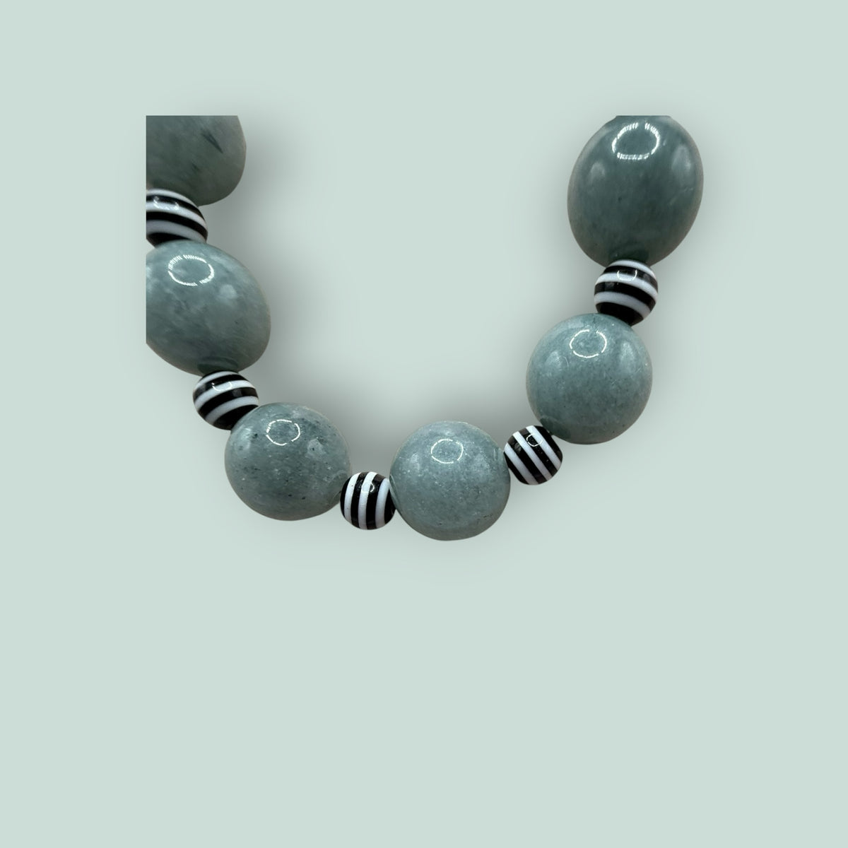 The Salty Bead Co handcrafted statement necklace featuring sage-green stone beads and black-and-white striped accents.