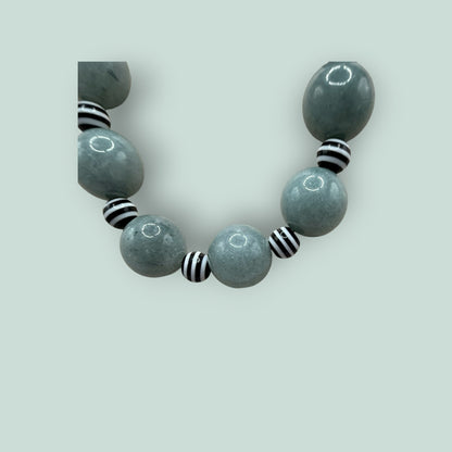 The Salty Bead Co handcrafted statement necklace featuring sage-green stone beads and black-and-white striped accents.