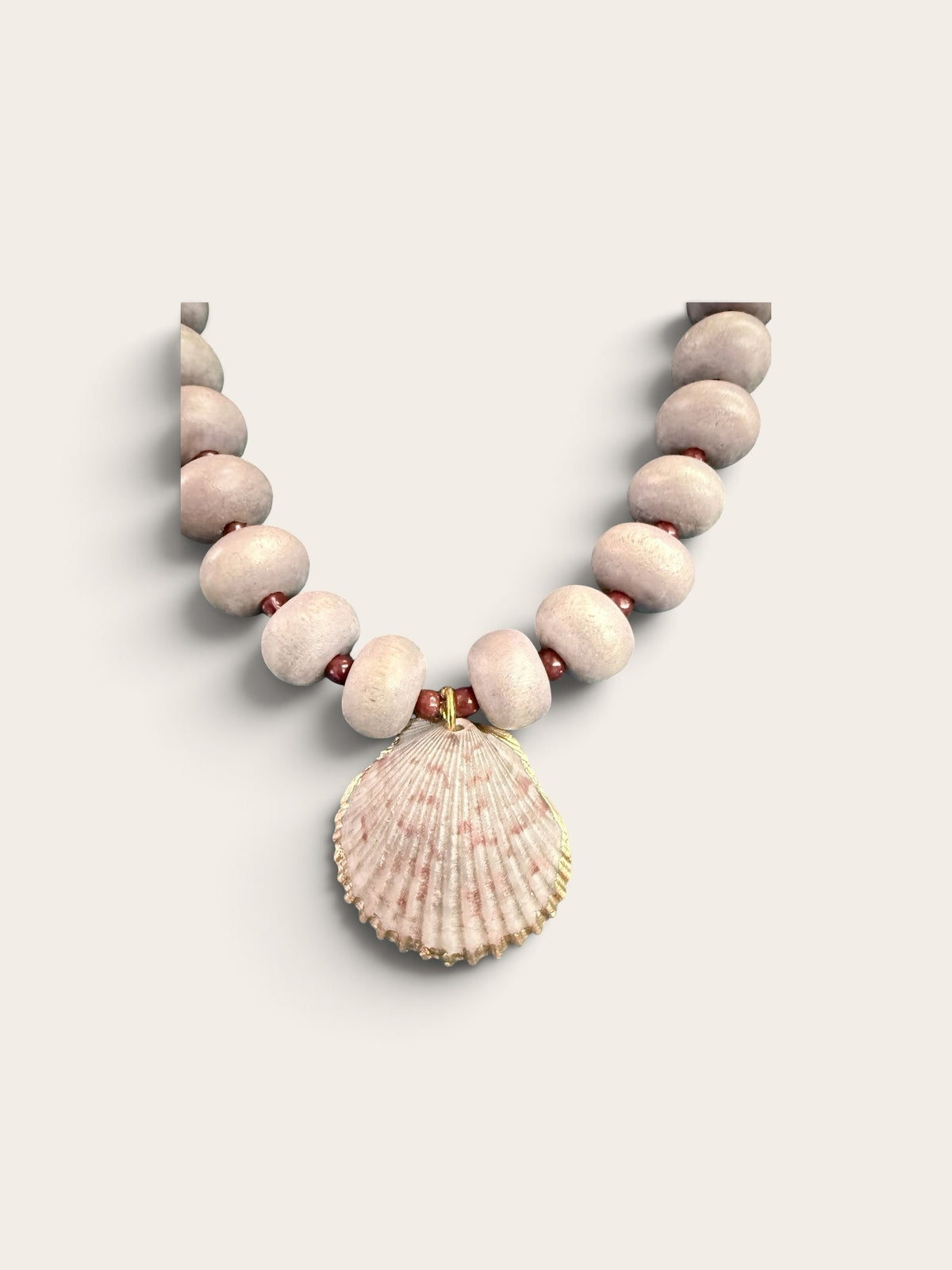 The Salty Bead Co coastal necklace with dusty-pink matte beads and a natural seashell pendant with gold-tone edging.