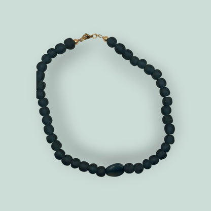 The Salty Bead Co handcrafted necklace with matte teal-blue beads and a polished oval stone centerpiece, gold clasp.