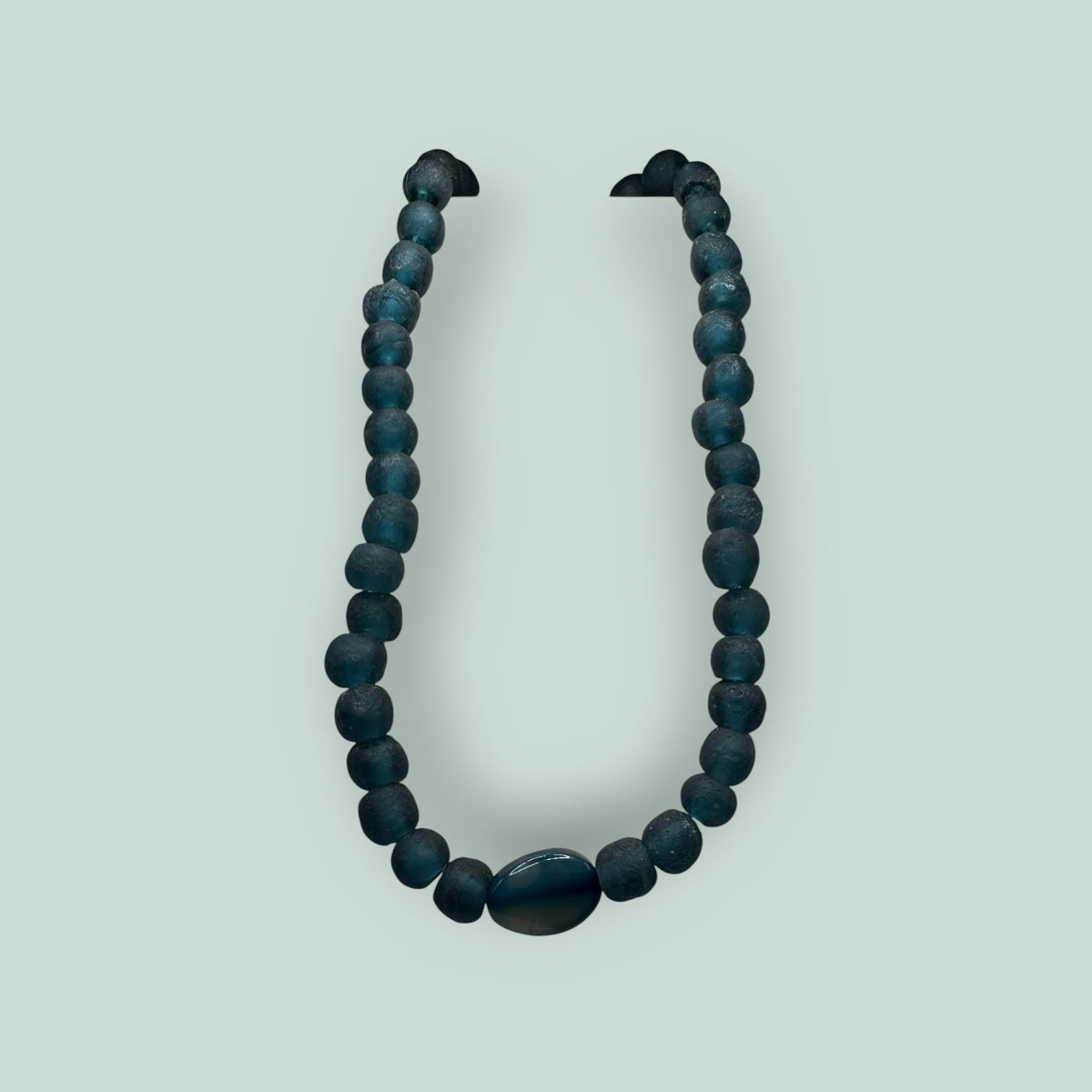 The Salty Bead Co handcrafted necklace featuring matte teal-blue beads and a polished oval stone centerpiece.