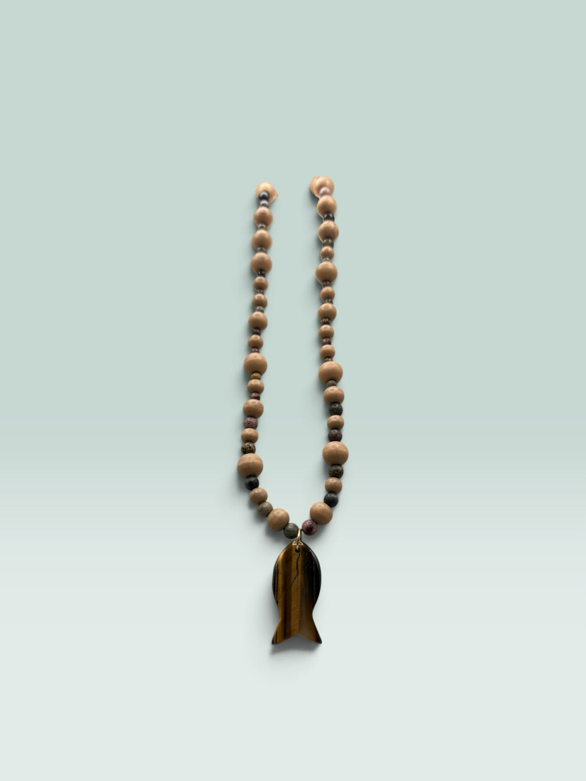 The Salty Bead Co handcrafted necklace with light wooden beads, dark stone accents, and a tiger's eye fish pendant.